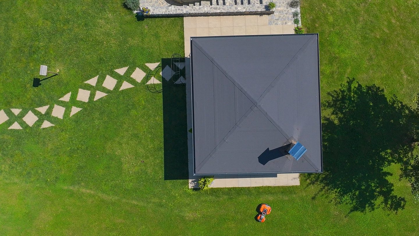 Drone view of a managed property: a slate-roofed building set in a manicured green lawn with stone walkways, the perimeter recently mowed by a Plowz and Mowz pro.