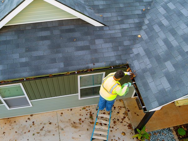 Plowz and Mowz pro on a ladder clearing autumn debris from a homeowner's gutters