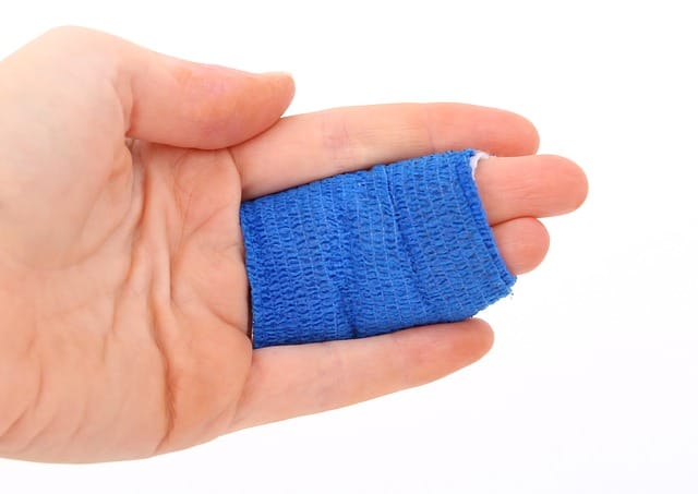 A hand is held up, palm up, with it's two middle fingers wrapped in a blue bandage.