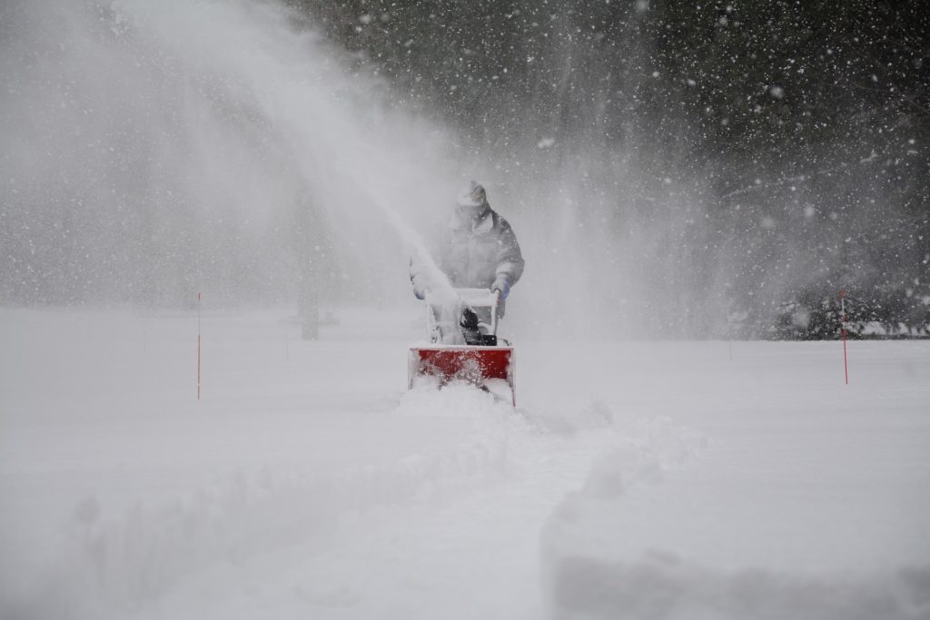 man snow blowing in winter storm
