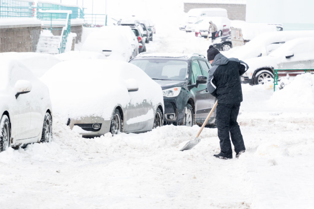 man shoveling car out of snow filled street